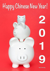 Happy Chinese New Year, the year of the pig with three piggy banks in various sizes stacked up on each other on red background. Happy Chinese New Year text