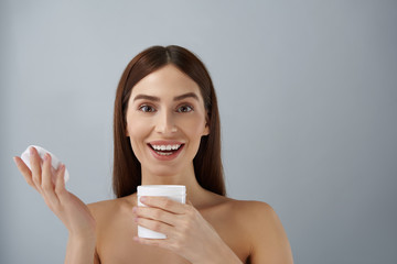 Happy young lady holding opened jar of cosmetic cream