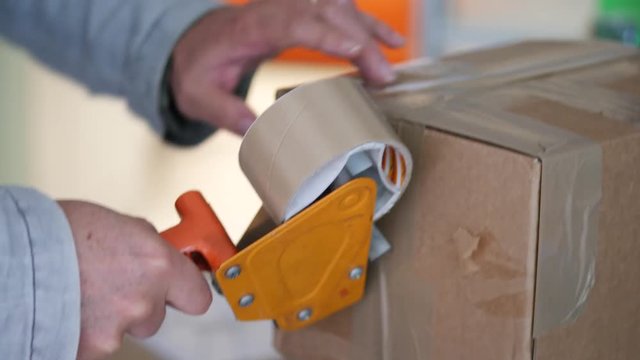 Hands putting self-adhesive tape with dispenser on brown cardboard box