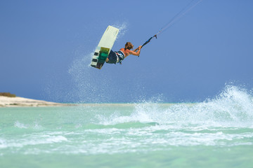 Professional kite boarding rider sportsman with kite in sky jumps high acrobatics kiteboarding trick with grab of kiteboard and huge water splash. Recreational activity, extreme active air sports