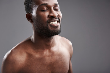 Close up of a delighted afro American man standing against gray background