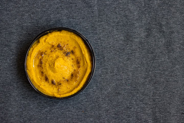 Chickpea yellow hummus with cumin and olive oil served in ceramic dark bowl in grey background. Arabian traditional food. Vegan vegetarian healthy dinner