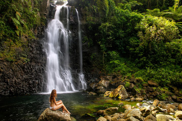 Young woman in bikini sitting by Middle Tavoro Waterfalls in Bouma National Heritage Park, Taveuni...