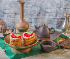 Tea break with a delicious strawberry cake and small chocolates. Copper and clay plates in a composition with jugs. Arab concept
