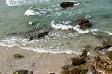 Fototapeta premium Green sea with wave splashing black rock and brown sand on the beach, Hua Hin , Thailand