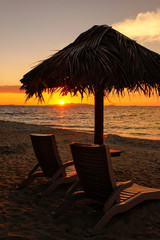 Silhouetted sun chairs with thatched umbrella on a beach at sunrise