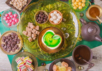 Tea break with a delicious honey cake decorated in the form of a green apple and a variety of multi-colored small candies. Copper and clay plates in a composition with jugs. Arab concept