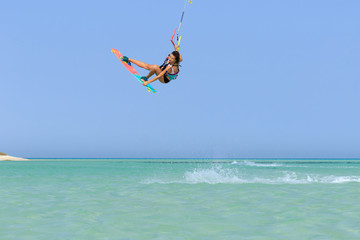 Kite surfing girl in sexy swimsuit with kite in sky on board in blue sea riding waves with water splash. Recreational activity, water sports, action, hobby and fun in summer time. Kiteboarding sport