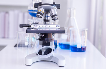 A microscopes in a lab with medical glassware.Its put on a table that have free space.