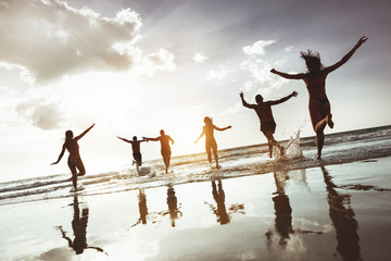 Big group of happy friends runs and jumps at sunset beach. Six active silhouettes against sea beach