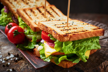 Homemade sandwich with ham, lettuce, cheese and tomato on a wooden background