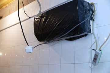The conditioner on the white tiled wall is covered with black plastic bag for the period of repair. Concept to keep equipment from dust during major repairs in the restaurant’s kitchen