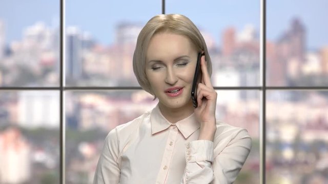 Cheerful emotional middle-aged blonde talking on phone. Beautiful playful business lady talking on cell phone. People, technology and communication concept.