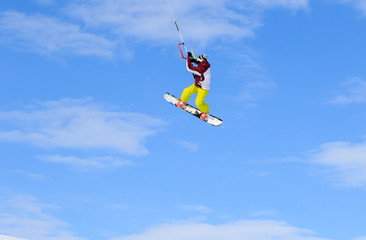 Fototapeta na wymiar Professional kite boarding rider sportsman with kite in sky jumps high acrobatics kite boarding trick with grab of kite board. Recreational activity, extreme active sports, snow kiting ski snowboard