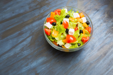 Greek salad in glass bowl on black or dark gray wooden or metal table