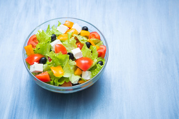 Greek salad in glass bowl on dark gray wooden or metal table