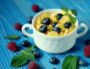Healthy eating, food and diet concept - Cornflakes with berries raspberries and blueberries on blue wooden background.