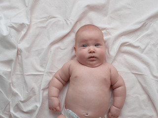 the baby lies carelessly and looks at the camera in surprise. The baby lies on a white linen cloth.