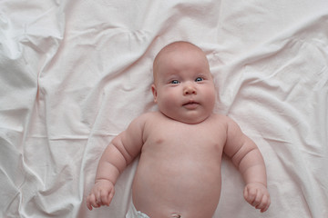 Happy and surprised blue-eyed baby. The baby lies on a white linen cloth.