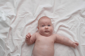 The baby with the face in bewilderment.The baby lies on a white linen cloth.