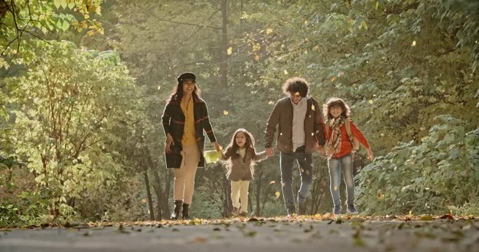 Young asian family of four walking down the road in golden autumn park, cheerfuly smiling - 4k