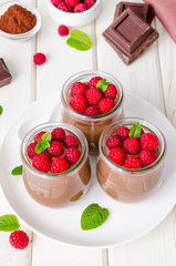 Chocolate pudding (mousse) with fresh raspberries in glass jars on a white wooden background. Dessert on Valentine's Day and Women's Day.
