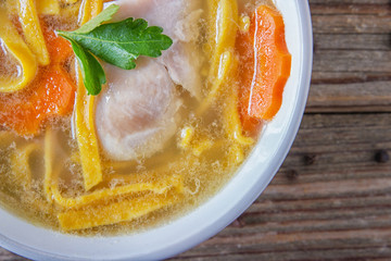 Homemade delicious chicken soup with noodles, carrots and onions in a ceramic bowl on a wooden table. View from above