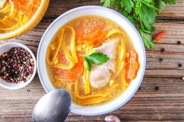 Homemade delicious chicken soup with noodles, carrots and onions in a ceramic bowl on a wooden table. View from above