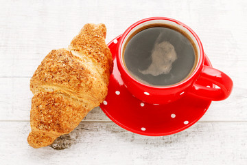 French croissant and cup of black coffee on white wooden table.