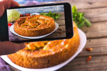 Hands with the phone takes pictures of a pie.Traditional homemade open pie with cabbage and sauerkraut on the plate on the rustic wooden background