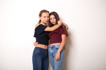 Two young girlfriends posing against wall