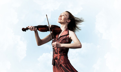 Woman violinist in red dress playing melody against cloudy sky