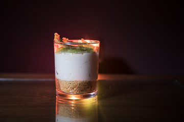 Sweet cheesecake in glass on a table with toned foggy backglight.