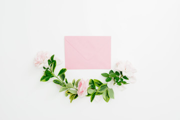 Floral composition of paper envelope with pink roses and green leaves on white background. Flat lay, top view