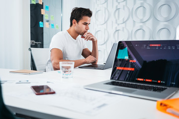 Young coworkers people working at work place office while sitting at table and analyzing trends on monitor screen. Business man and woman analyze document and blueprint plan