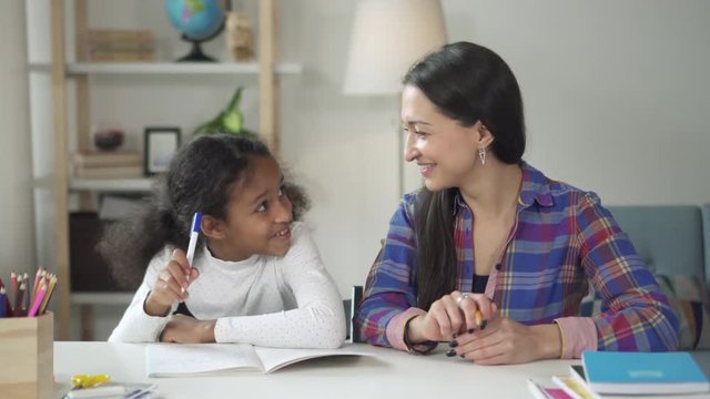 Caucasian teacher is helping to mixed-race girl in school. Encouraging support on working hard and good learning in classroom. Cheerful pupil smile and laugh getting knowledge together with tutor.