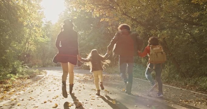 South asian family of four running in autumn park with golden leaves, happily smiling and looking at each other - young family concept 4k