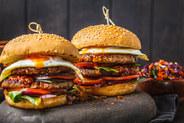 Homemade pork burgers with egg, sauce and vegetables on dark background.