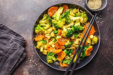 Vegan wok stir fry with broccoli and carrot in black dish, top view, copy space.