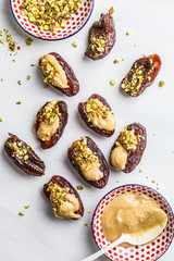Dates stuffed with peanut butter, chocolate and pistachios on white background.