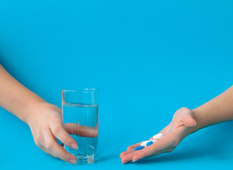 Hands holding pills and water on a blue background