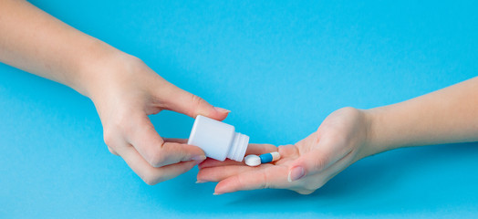 Hands holding white bottle for pills and pills on a blue background