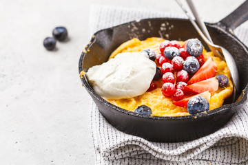 Dutch baby pancake with berries and cream in a cast-iron pan.