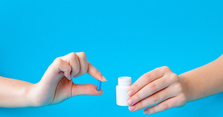Hands holding white bottle for pills and pills on a blue background