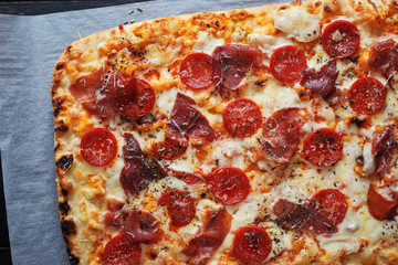 Homemade hot traditional Italian pizza with pepperoni , cheese and prosciutto top view