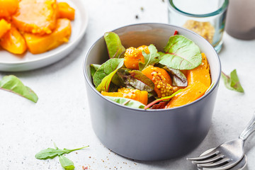 Green salad with pumpkin and mustard in gray bowl. Healthy vegan food concept.