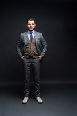 Full length portrait of a fashion male model over black background. Looking at camera.