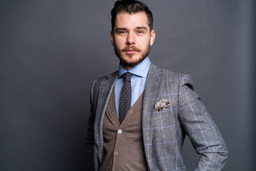 A confident elegant handsome young man standing in front of a grey background in a studio wearing a nice suit.
