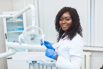 Abwaschbare Fototapete Zahnärzte Porträt des weiblichen schwarzen Zahnarztes in der Zahnarztpraxis. Sie steht in ihrem Büro und sie hat ein schönes Lächeln.