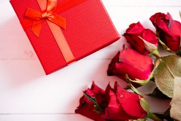 Red flower roses and gift box on white wooden background,